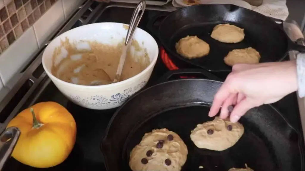 adding chocolate chips to sourdough pumpkin pancakes in a cast iron skillet