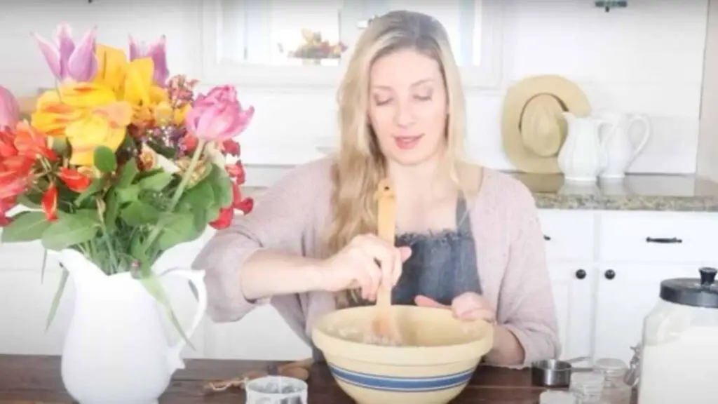 woman hand stirring batter for carrot cake in a mixing bowl with a bouquet of spring flowers