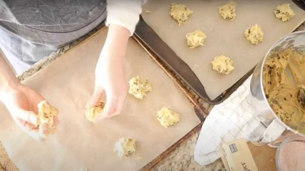 dropping sourdough chocolate chip cookie dough onto parchment paper lined baking sheets