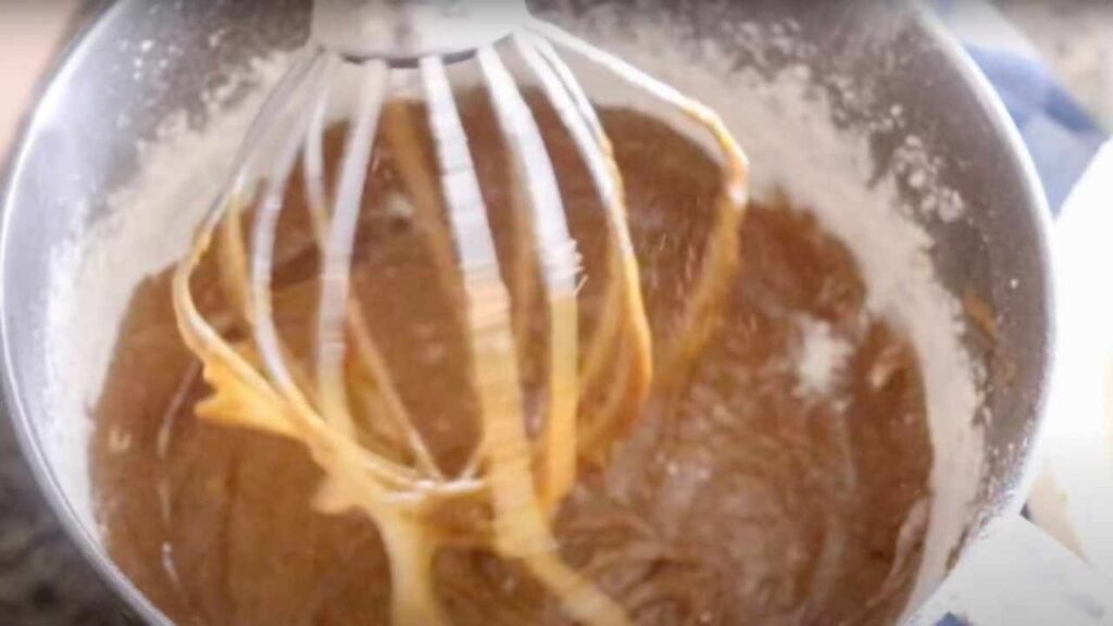 wet and dry ingredients for carrot cake in the bowl of a stand up mixer with whisk attachment