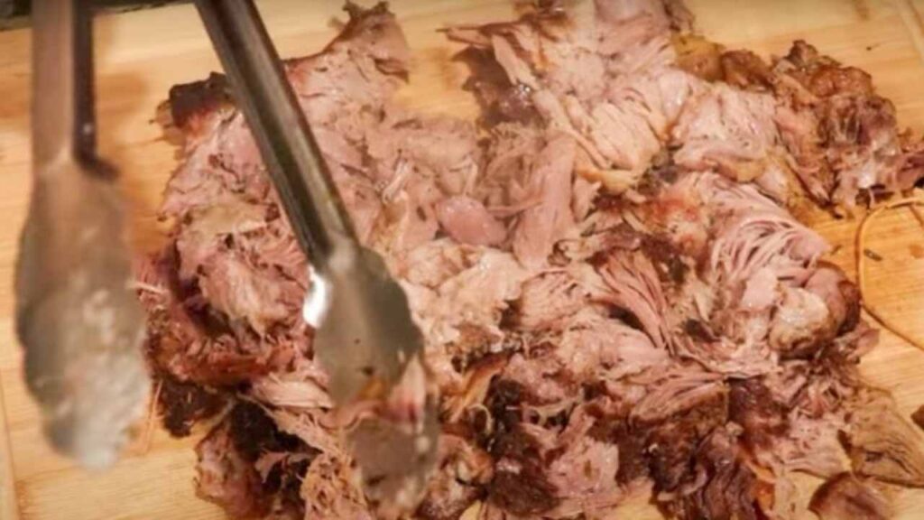 tender pork shoulder roast being shredded with tongs