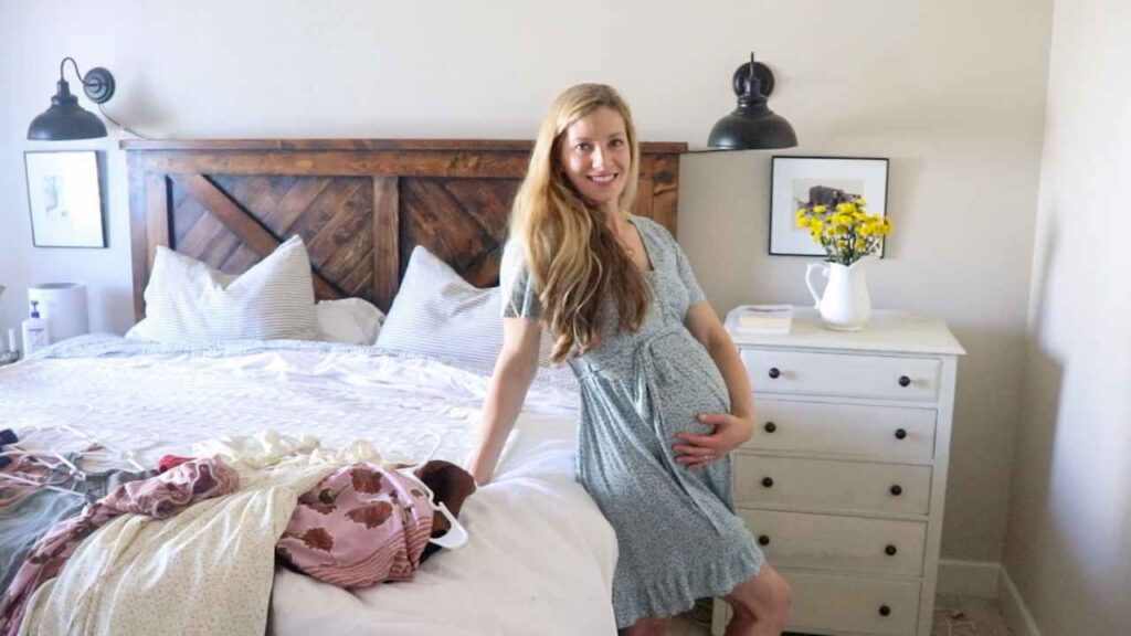 girl sitting on bed modeling a blue green maternity dress