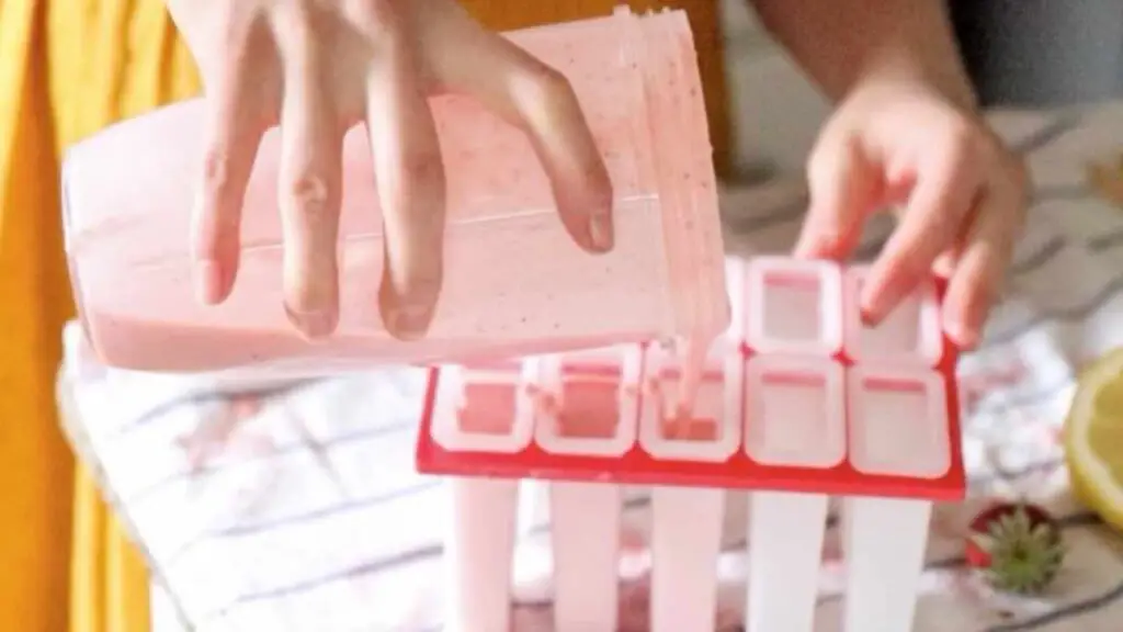 pouring strawberry cream kefir mixture into popsicle molds
