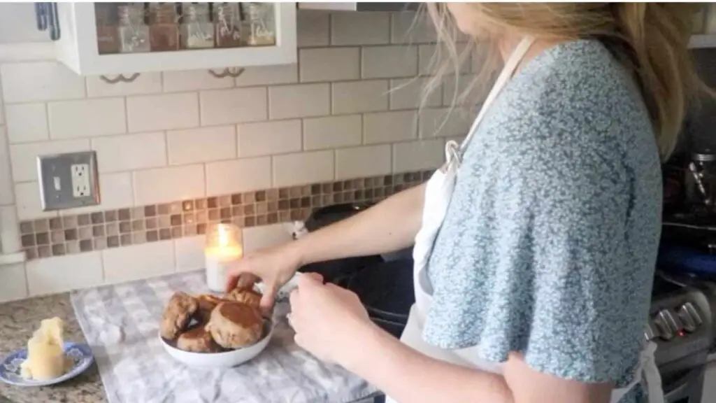 woman placing fresh whole wheat sourdough English muffins in a bowl