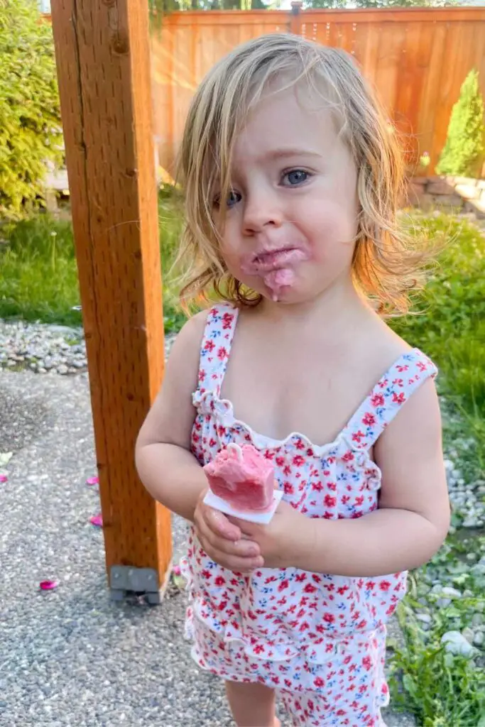toddler girl enjoying a strawberry cream kefir popsicle in the backyard