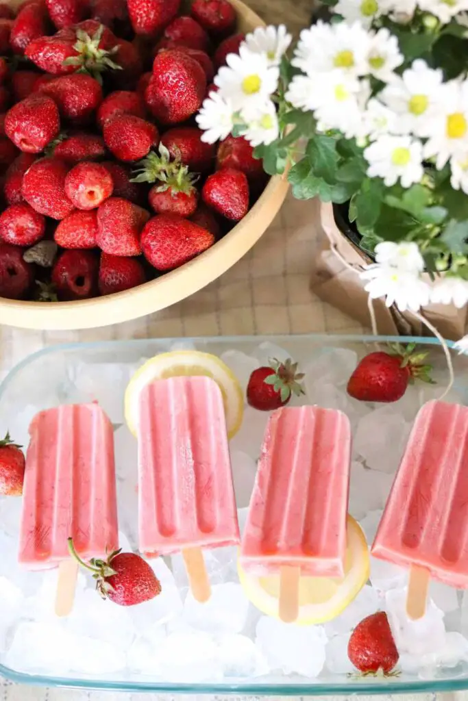 strawberry cream kefir popsicles in a dish of ice with daisies and strawberries