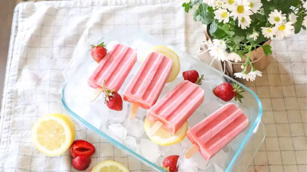 strawberry cream kefir popsicles in a dish of ice with daisies and strawberries