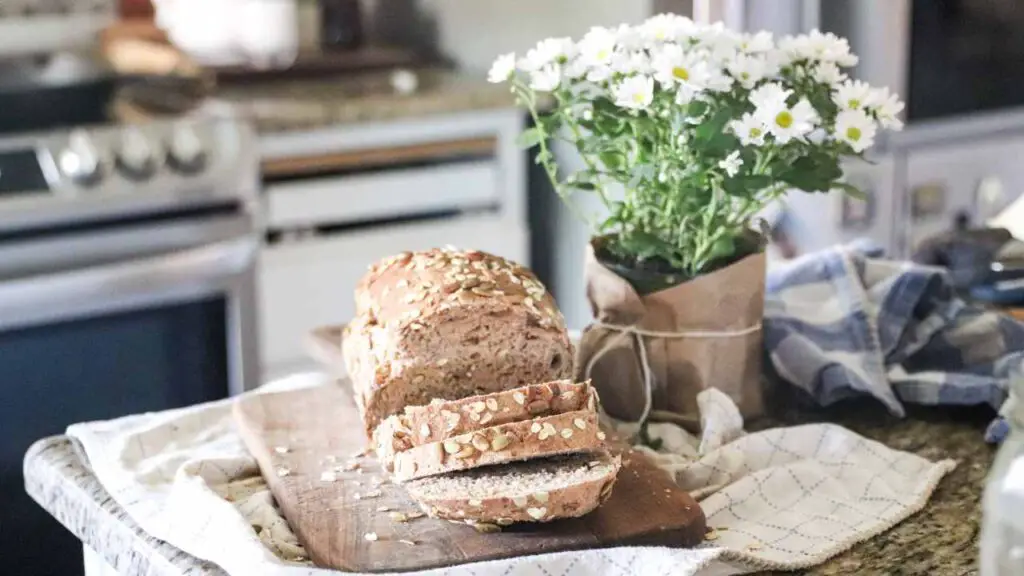 sliced fresh loaf of whole wheat seeded sourdough sandwich bread next to a bouquet of daisies on a kitchen counter