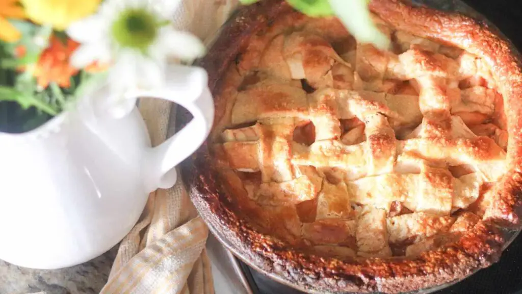 fresh baked apple pie with einkorn sourdough lattice crust and a white pitcher of summer flowers