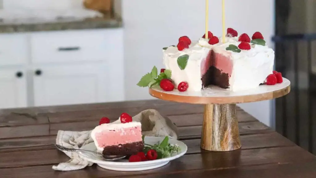 Homemade ice cream cake on a pedestal cake stand with birthday candles, and a slice of cake on plate