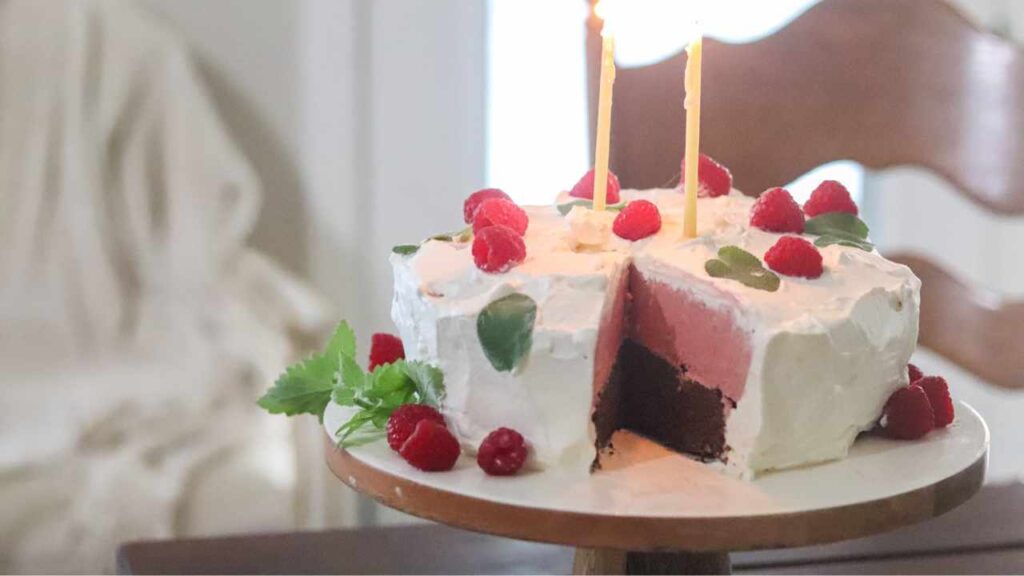 Homemade ice cream cake on a pedestal cake stand with birthday candles