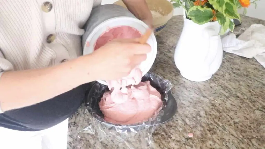 Scooping homemade raspberry ice cream into a lined cake pan