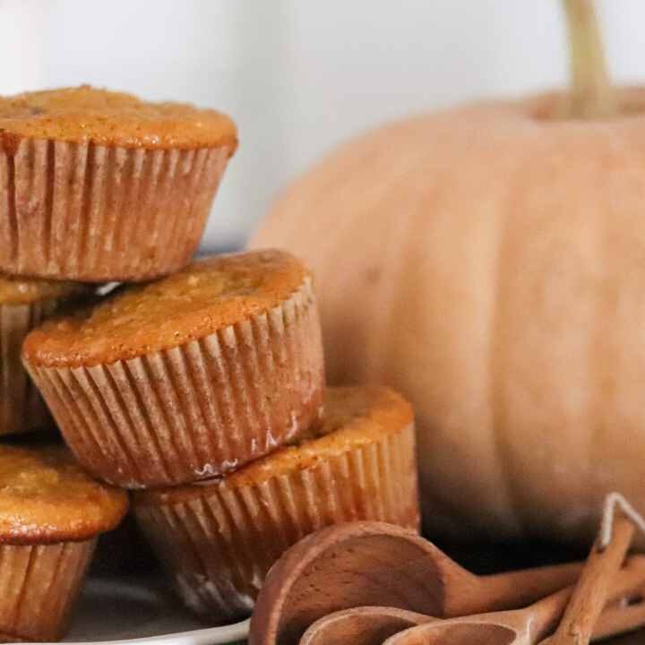 a stack of pumpkin protein einkorn muffins with a pumpkin in the background