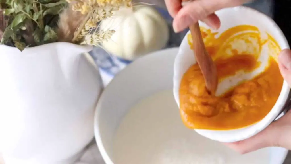 scooping pumpkin puree into a bowl with other ice cream ingredients