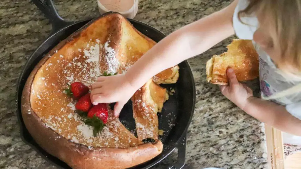A child reaching to grab a slice of dutch baby pancake from a skillet