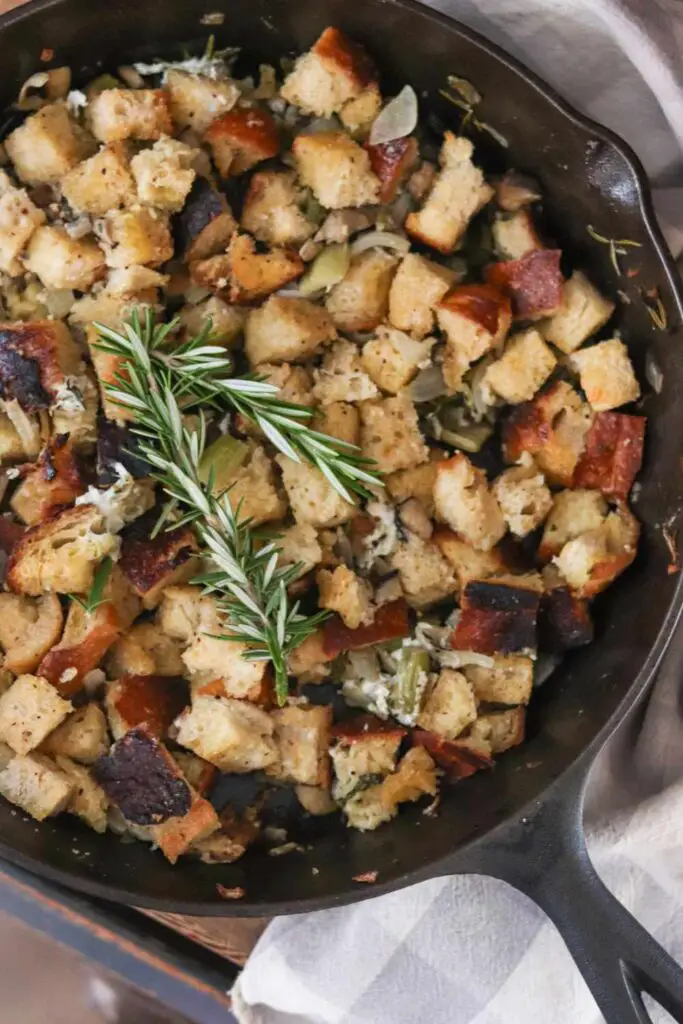 A cast iron skillet with sourdough stuffing and fresh rosemary in it