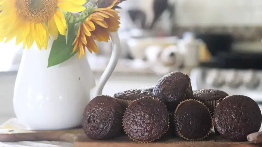 chocolate muffins on a wooden cutting board with sunflowers to the side