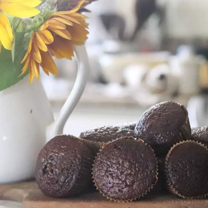 chocolate muffins on a wooden cutting board with sunflowers to the side