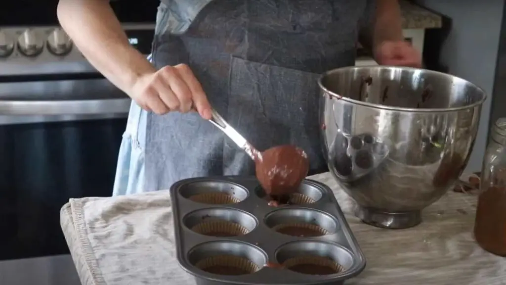 spooning chocolate muffin batter into muffin tins