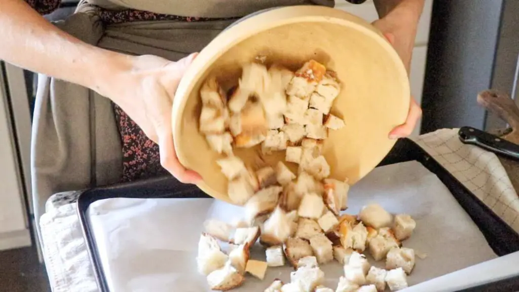 pouring bread cubes onto a parchment lined baking tray