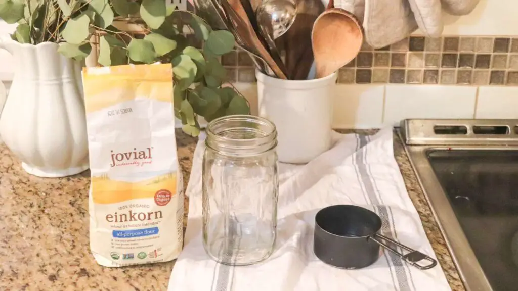 a bag of flour, a jar, and a measuring cup to make einkorn sourdough starter