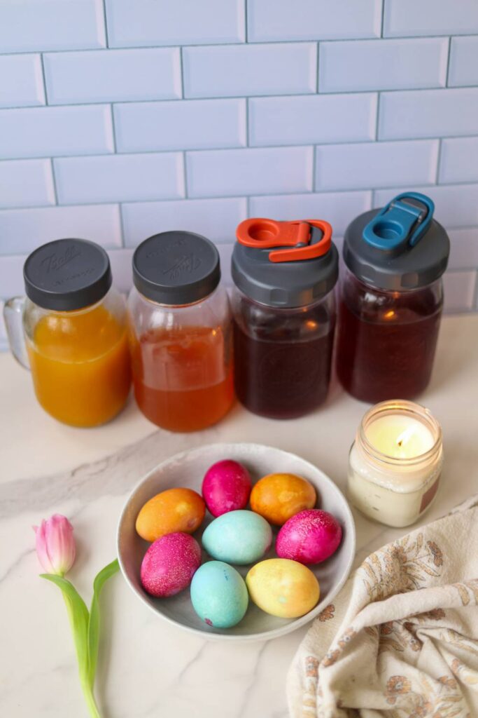Bowl of naturally dyed Easter eggs with jars of homemade dye in the background