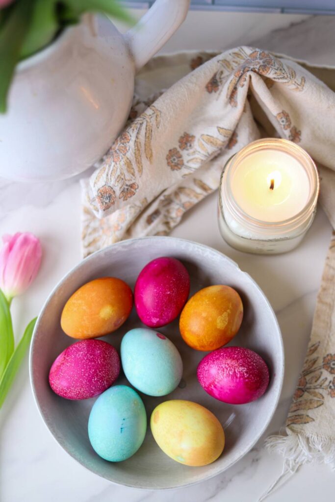 Bowl of naturally dyed Easter eggs with candle and kitchen decor