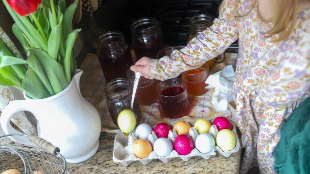 Child dipping eggs into natural dye jars on the counter