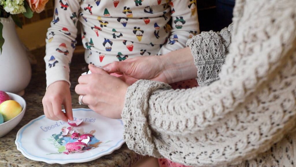 Adult helping a child peel a dyed Easter egg at the kitchen counter