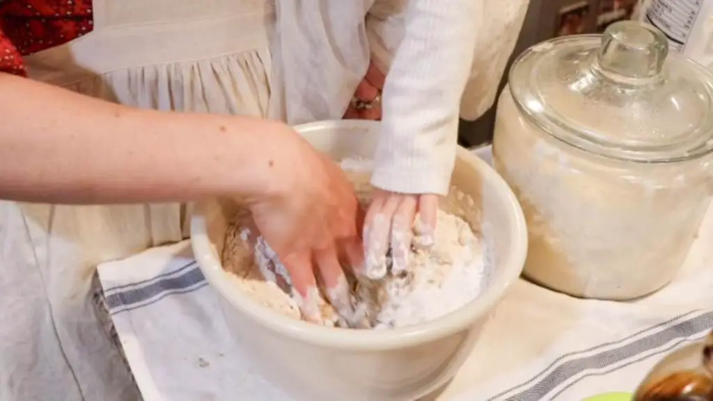 A mother and child kneading sourdough rye sandwich bread dough with their hands.