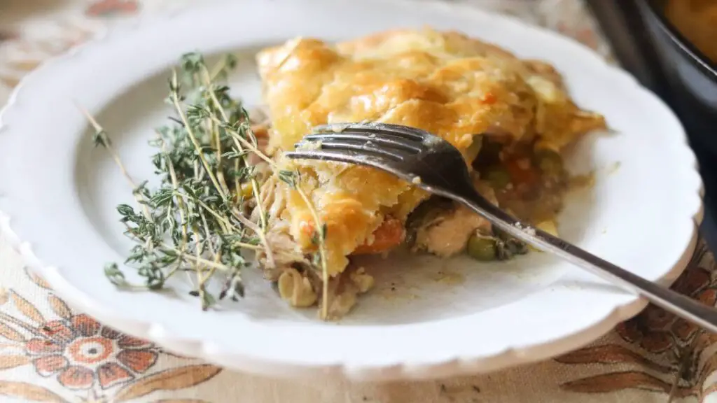 A slice of einkorn sourdough chicken pot pie on a white plate with a sprig of thyme.