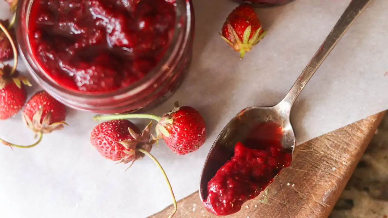 A jar of strawberry jam with a spoonful of strawberry jam and fresh strawberries.