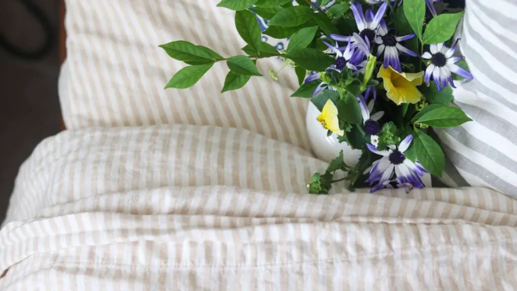 Looking down on Quince linen sheets on a bed with fresh flowers laying on them.