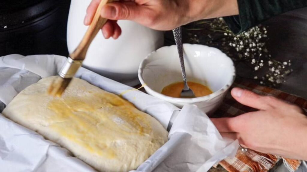 Brushing a loaf of sourdough sandwich bread with egg wash before baking it. 