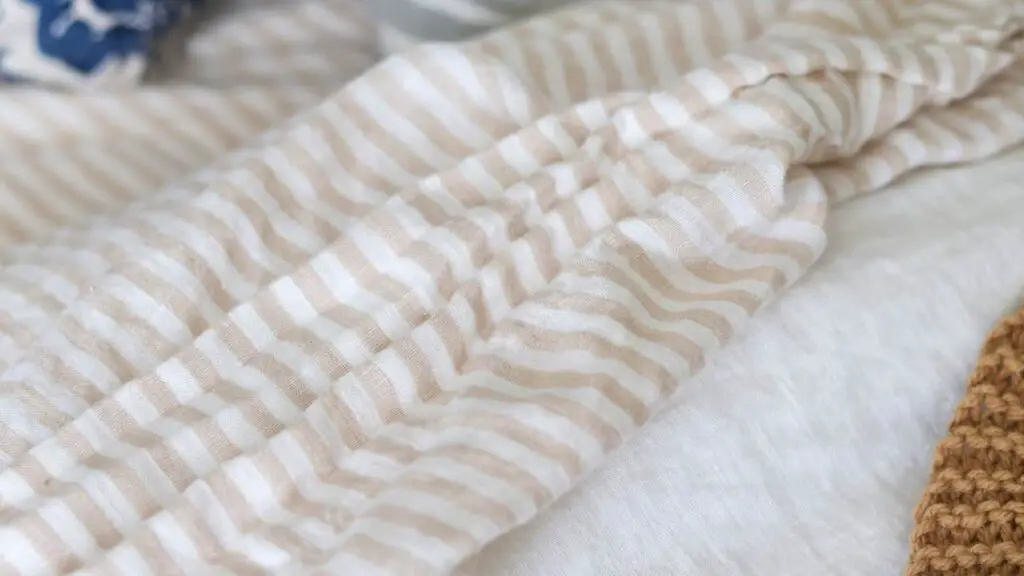 Quince linen sheets in beige and tan stripes pattern on a bed. 