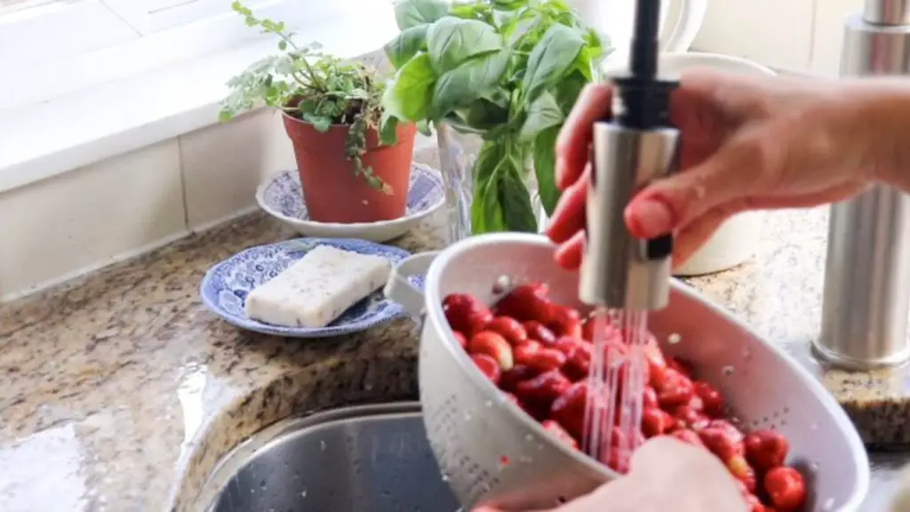 Rinsing strawberries in the sink in a metal colander. 