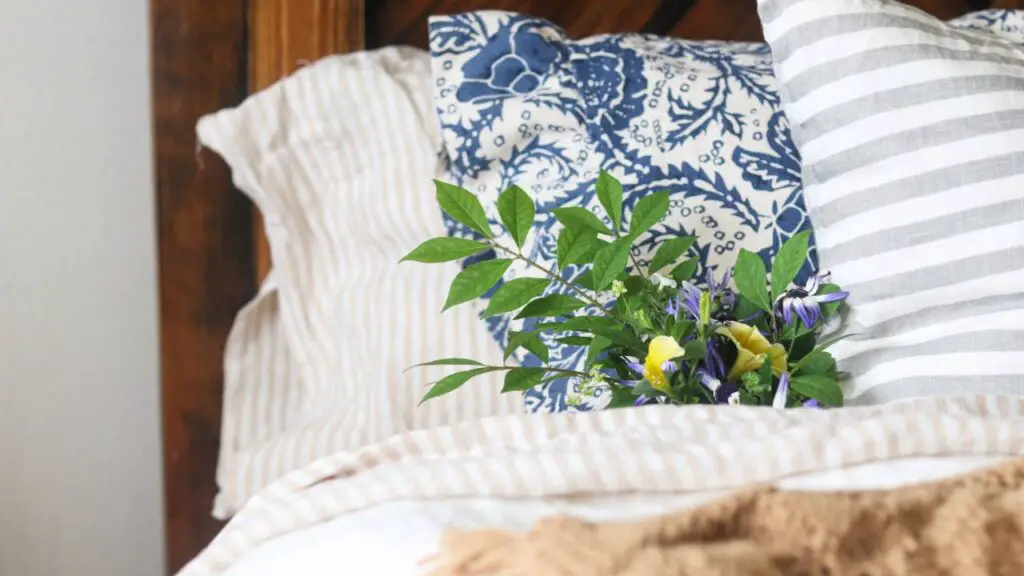 A bed made with Quince linen sheets in a beige and white striped pattern with fresh flowers on the pillow. 