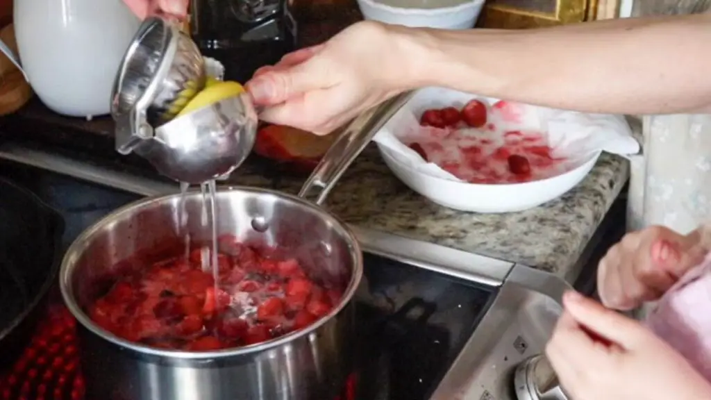 Squeezing a lemon into a pot of strawberry jam. 