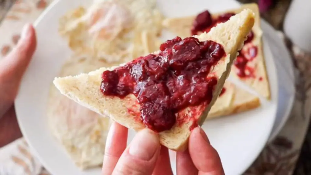 A piece of sourdough sandwich bread with strawberry jam smeared on it. 