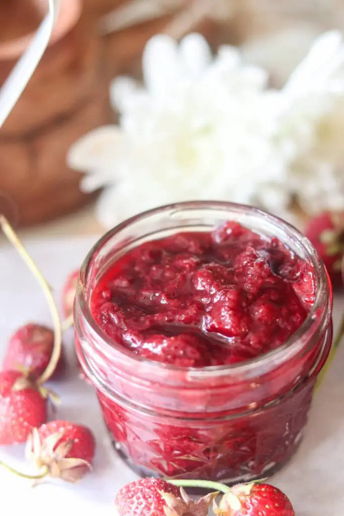 A jar of strawberry jam with fresh strawberries. 