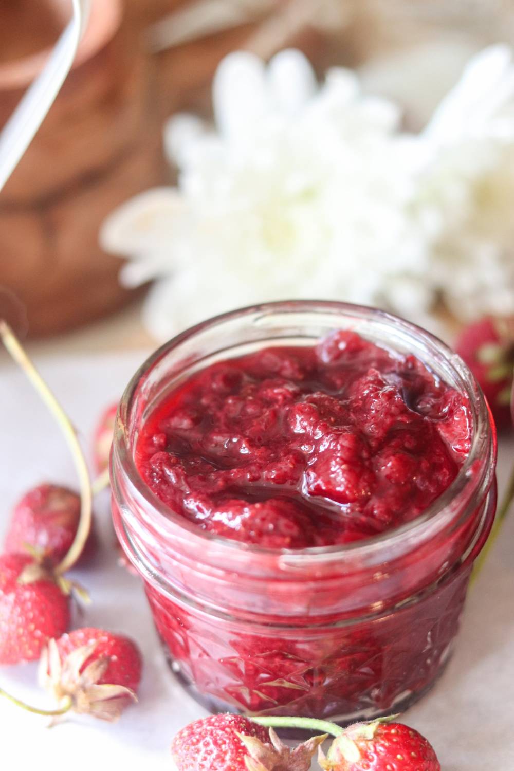 A jar of strawberry jam with fresh strawberries.