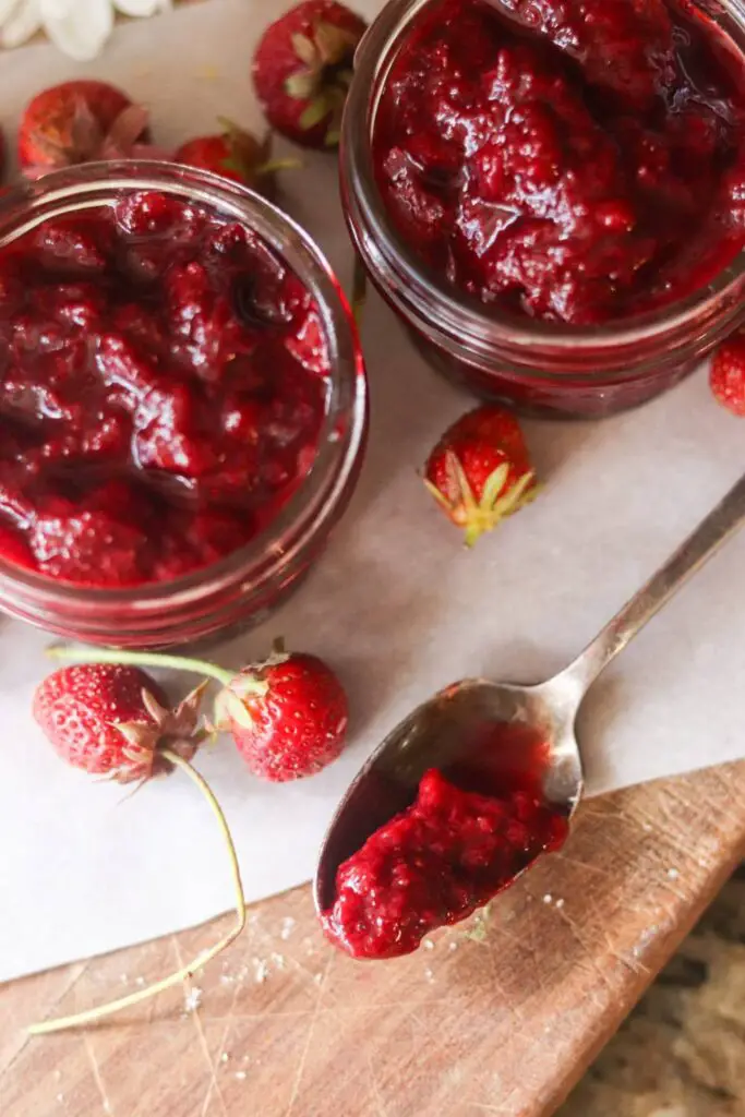 Two jars of strawberry jam with a spoonful of strawberry jam and fresh strawberries.