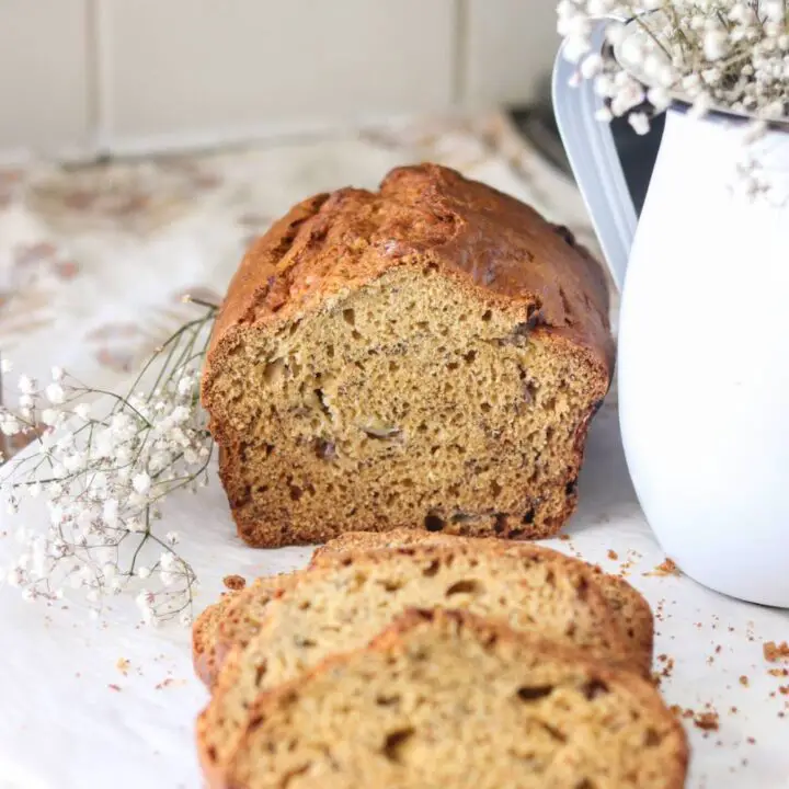 A sliced loaf of einkorn sourdough banana bread on a white countertop with flowers beside it.