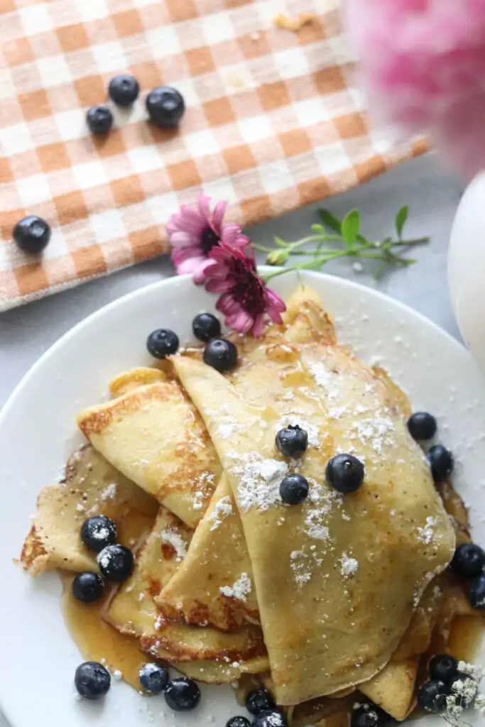 Looking down on a plate of sourdough crepes with fresh blueberries and pink flowers.