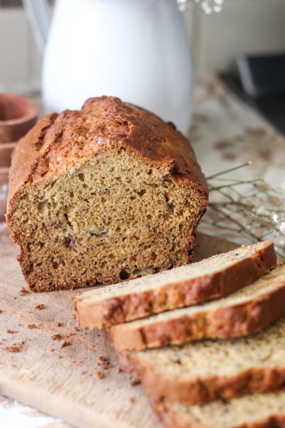 A sliced loaf of einkorn sourdough banana bread on a white countertop with flowers beside it.