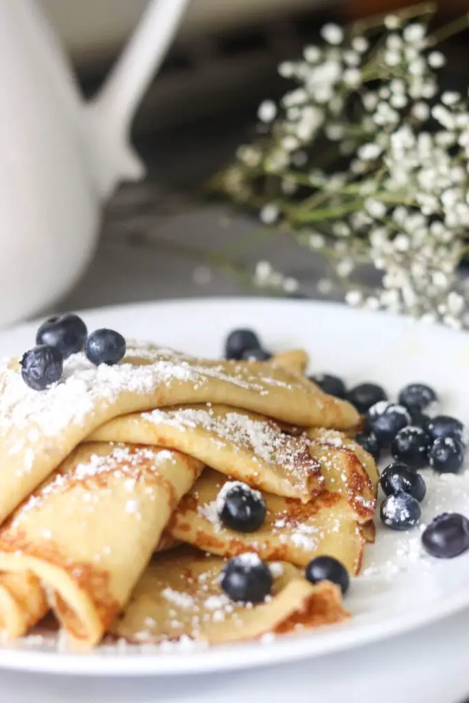 A stack of sourdough crepes on a white plate with fresh blueberries.