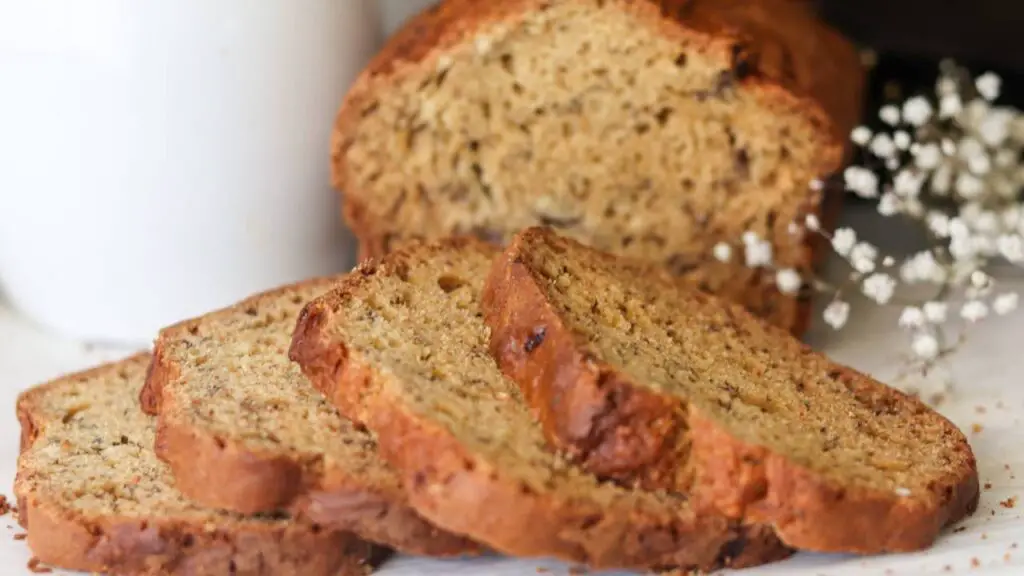 A sliced loaf of banana bread with flowers behind it. 