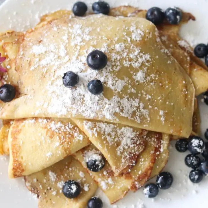 A plate of sourdough crepes with fresh blueberries and powdered sugar on top.