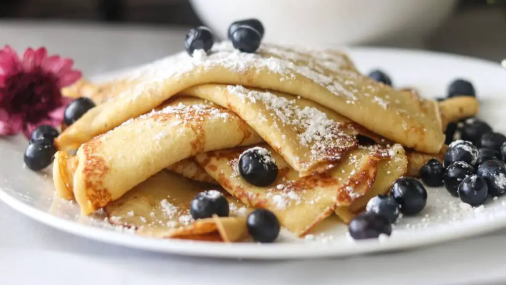 A plate of sourdough crepes with fresh blueberries and powdered sugar on top.