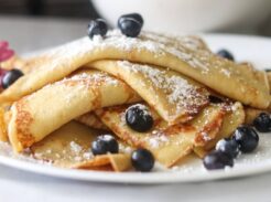 A plate of sourdough crepes with fresh blueberries and powdered sugar on top.